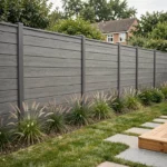 Clôture de jardin en composite gris anthracite installée le long d'une pelouse soignée avec allée en pierre et terrasse en bois