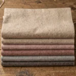 Échantillons de tissu en flanelle coton plié soigneusement sur une table en bois, montrant différentes teintes douces et textures naturelles