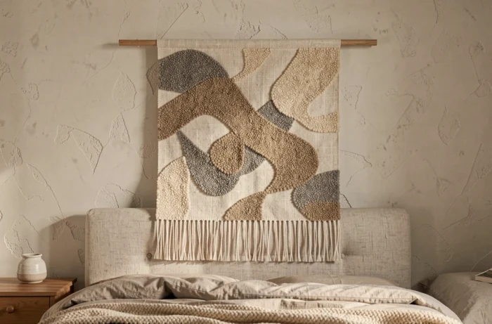 Textile mural tissé à la main en lin et laine bouclée aux tons naturels suspendu à une tringle en bois dans une chambre apaisante